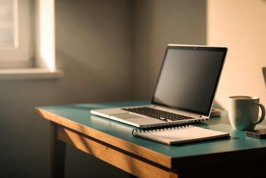 Image of a laptop sitting on a desk with a notebook and coffee cup beside it