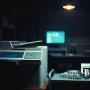 A legacy multi function printer sits next to a patient wrist band printer.  A single computer screen is lit up in the dark background.